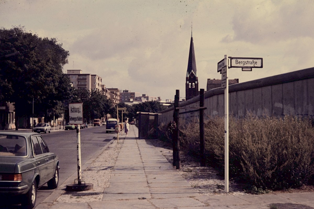 Berlin, 1985 – Gedenkzeichen und Bushaltestelle vor der Grenzmauer der Bernauer Straße (Fotograf: Conrad Bicker)
