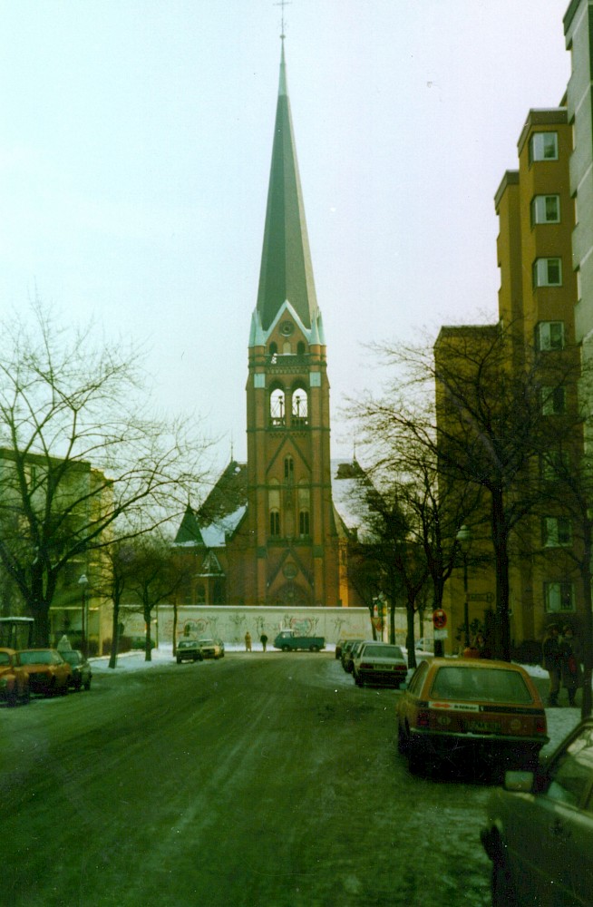 Berlin, ca. 1984 – Blick auf die Versöhnungskirche hinter der Grenzmauer und die von PKW beparkte Hussitenstraße (Fotograf: )